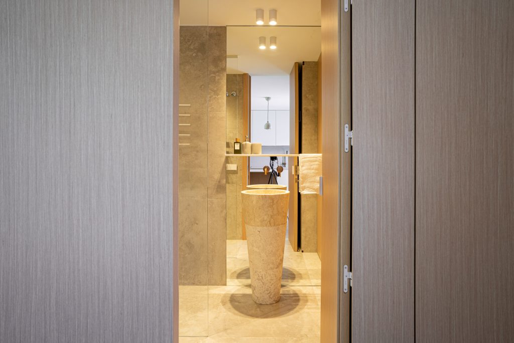 Lavabo de mármol beige con grifería dorada en baño entre puertas de madera