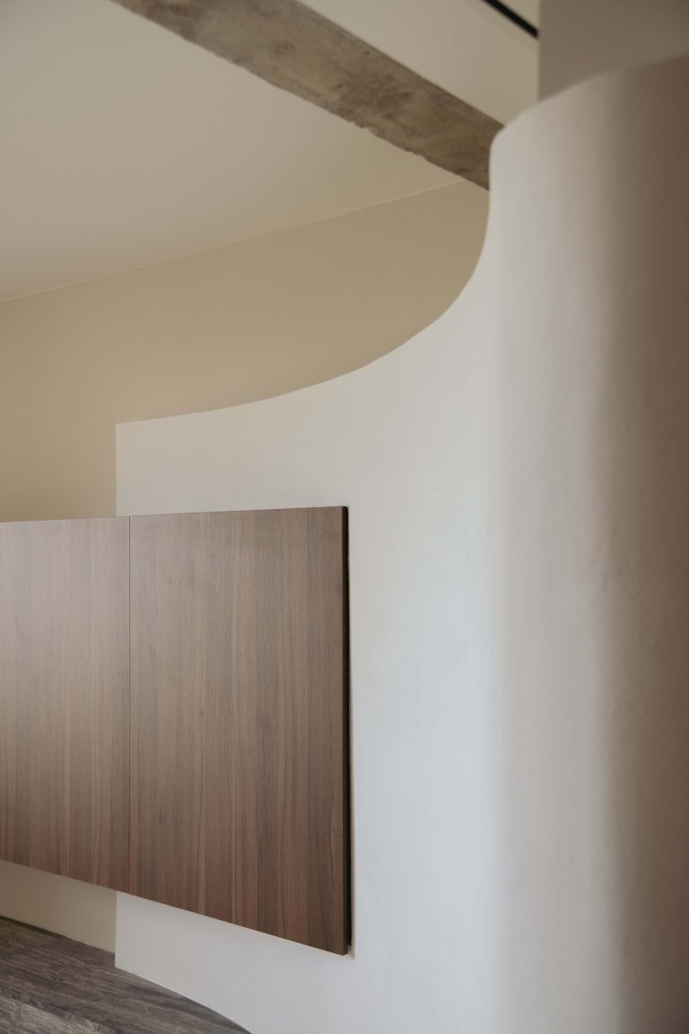 Detalle de pared curva blanca con mueble de madera suspendido en proyecto de interiorismo moderno.